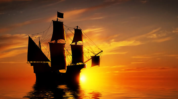 A traditional tall boat on an all inclusive cruise holiday sitting high on the ocean at sunset.