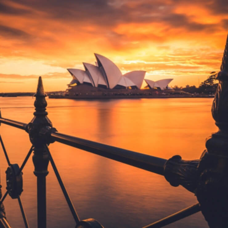 View of the sydney opera house from the syndey harbour bridge, wiht the sun setting orange over the water.
