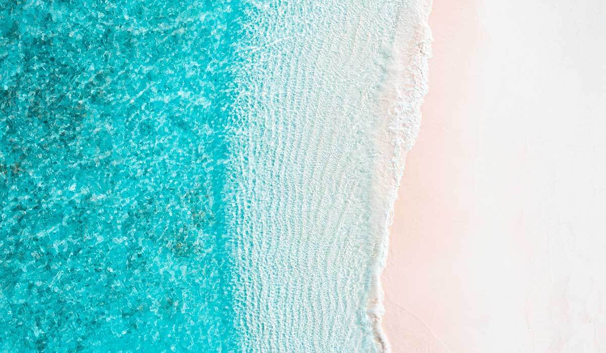 Aerial view of the clear turquoise ocean lapping waves on a white sand beach.