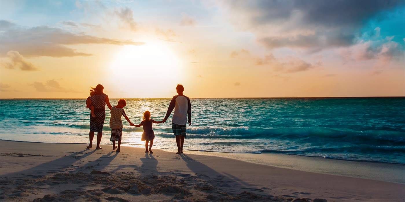 A family of four walking along a beach watching the sunset on a family holiday.