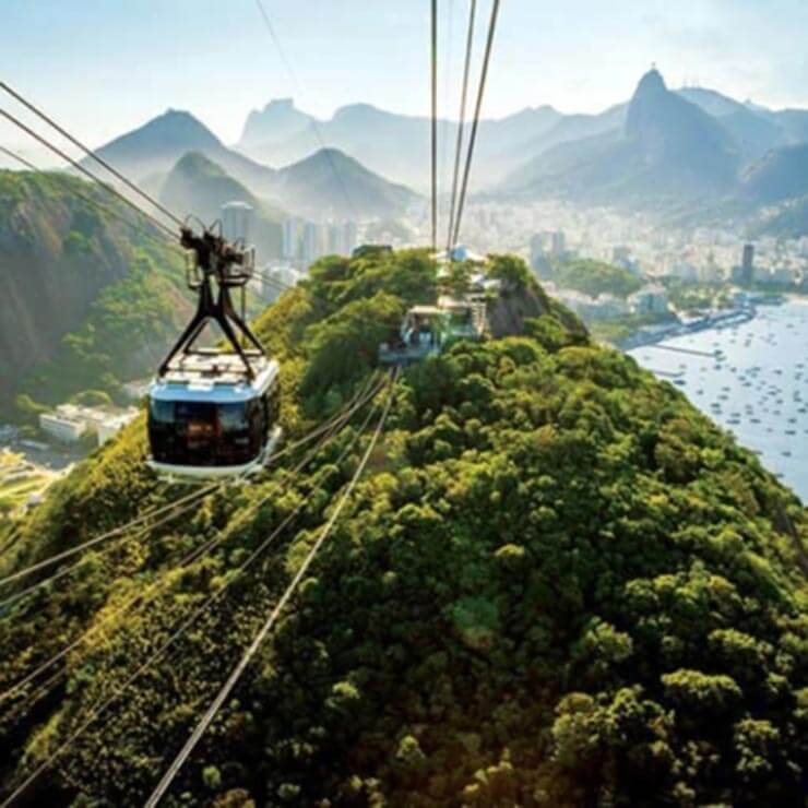 Cable cars over the green mountains of Brazil with the sea in the distance.