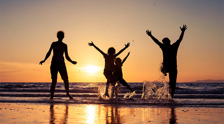 A group of friends dancing on the beach at sunset, silhouetted by the sun, during a bucket list birthday trip.