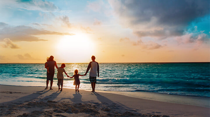 Parents and two children holding hands as they walk along the beach on their bucket list holiday.