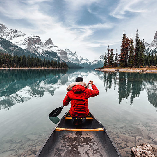 A man paddling his canoe towards a breathtaking snowy mountain view.