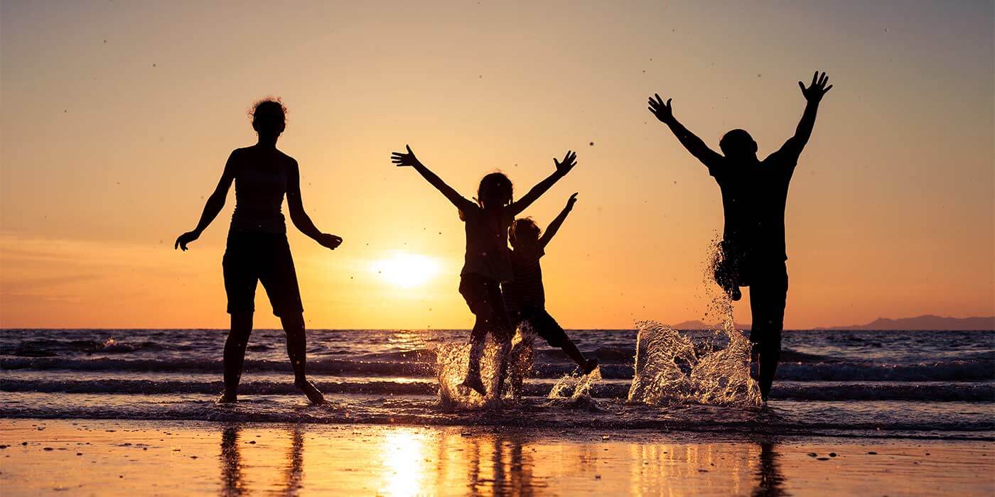 The sun setting on the beach as three friends dance and celebrate at one of the top birthday holiday destinations.