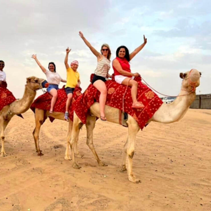 Sitting on red-blanket covered camels for tourist rides.