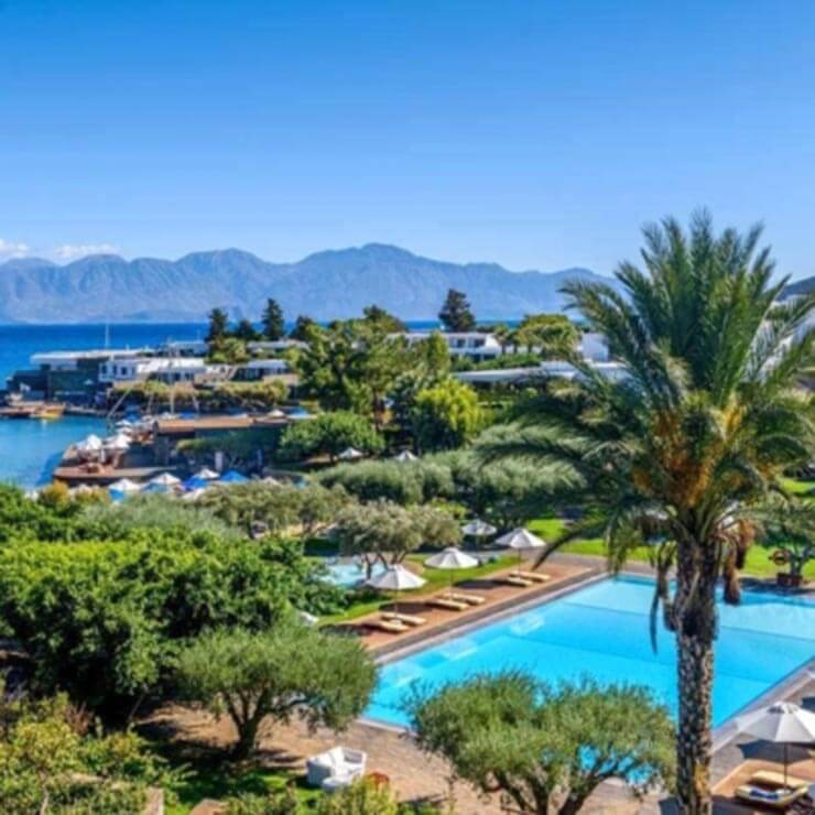 High end resort in the Greek Islands, with a luxury pool and view out to sea through the palm trees.