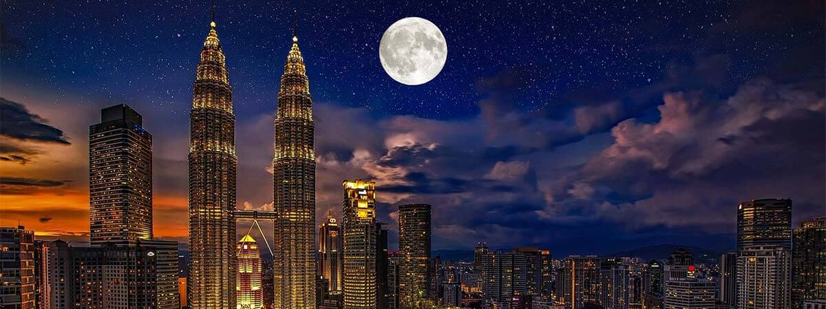 The moon high in the sky above the lit up cityscape of kuala lumpur on holiday in malaysia.