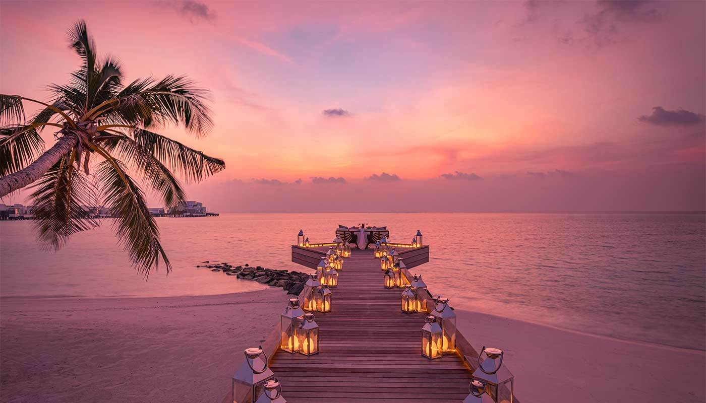 Luxurious sea jetty walkway set up for a wedding ceremony with candles and flowers, with the pink setting sun.