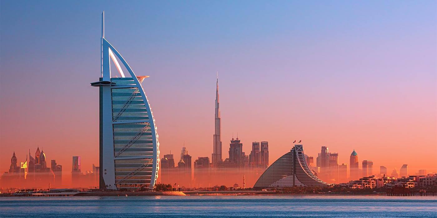 The stunning view of Dubai City and Burj Al Arab, the iconic luxury holiday resort, with a pink hue at sunset.