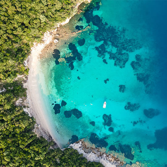 Beautiful crystal clear waters lapping a white beach in the Mediterranean, lined with green trees.
