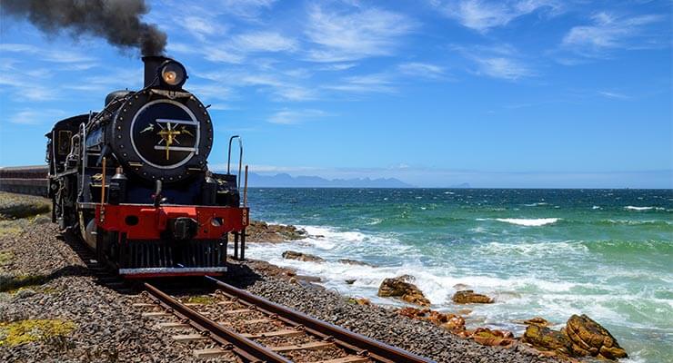 A black steam train running alongside the coastal waters on a rail holiday.
