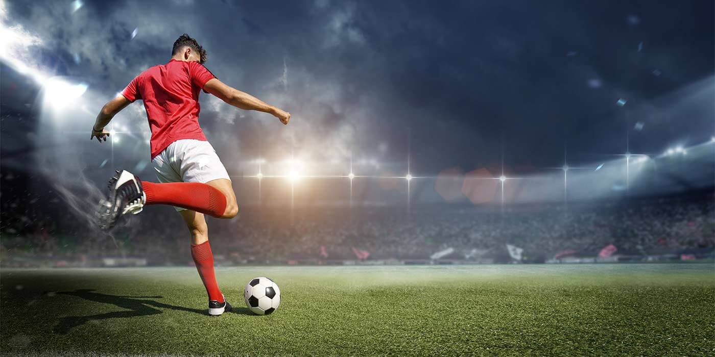 A soccer player kicking the ball towards the goal at a football game in Europe.