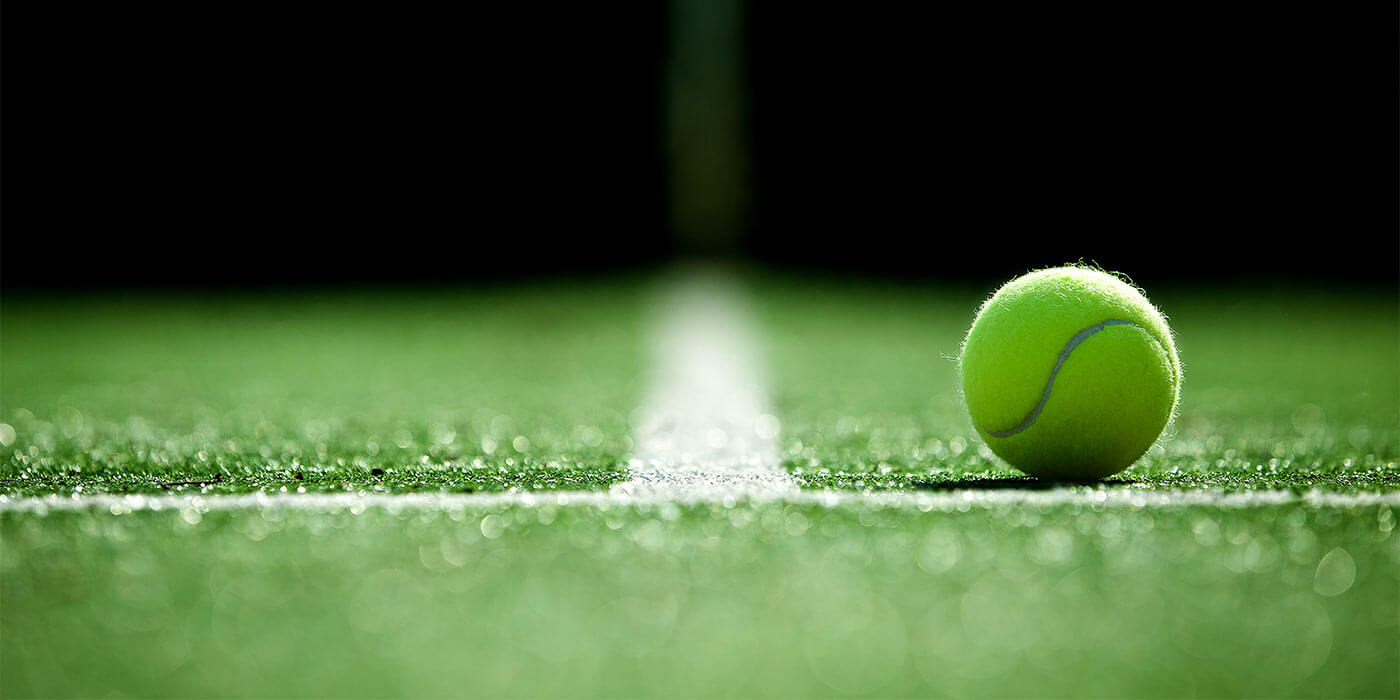 A tennis court at Wimbledon, a popular choice for sports holidays, with a close up view of a tennis ball on the border lines of the court.