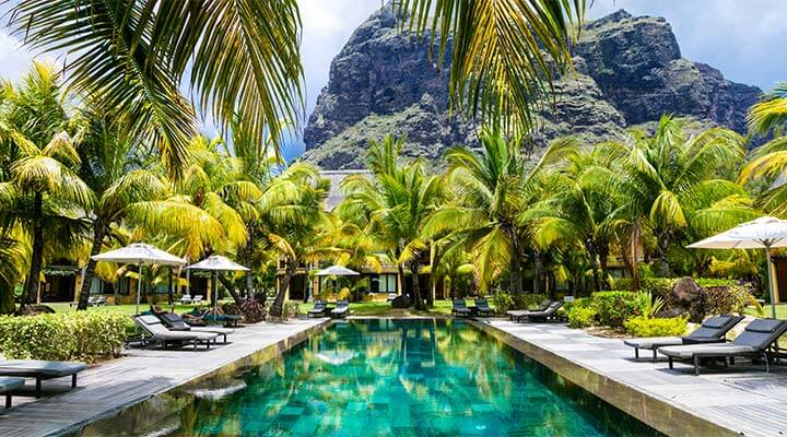 A breathtakingly beautiful pool, surrounded by lush palm trees and sun loungers at a bucket list destination.