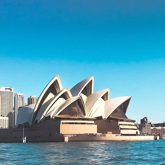 The Sydney Opera House on a sunny day with blue waves lapping the base.