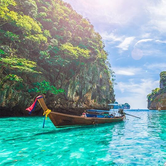 A thai longboat moored in crystal clear water near a lush green island.