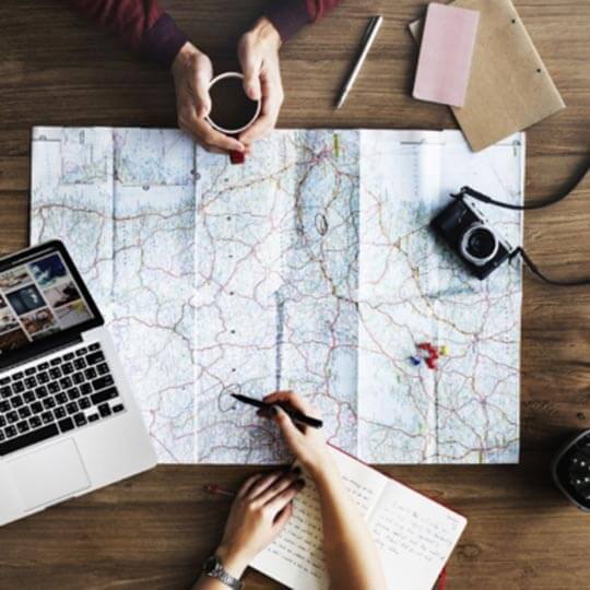 A map on a table surrounded by travel planning tools.
