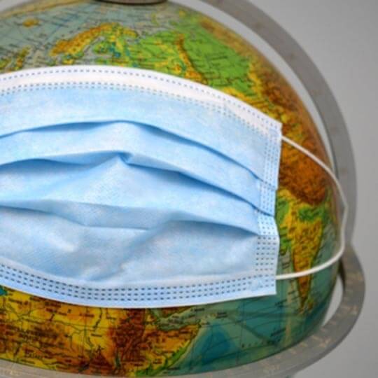 A covid face mask around a globe of the world.