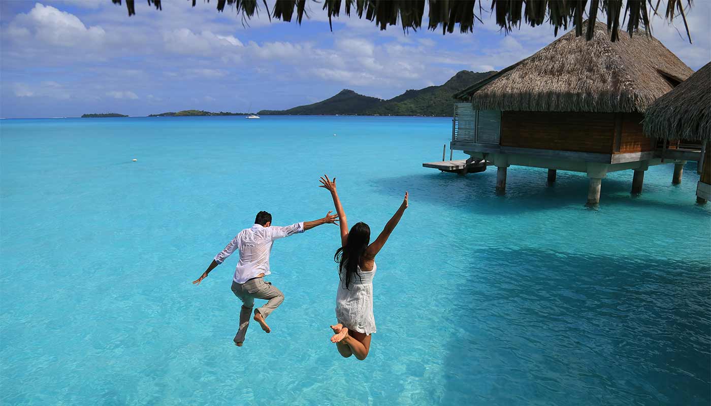 Recently married couple jumping into the sea in celebration for their honeymoon on a tropical island.