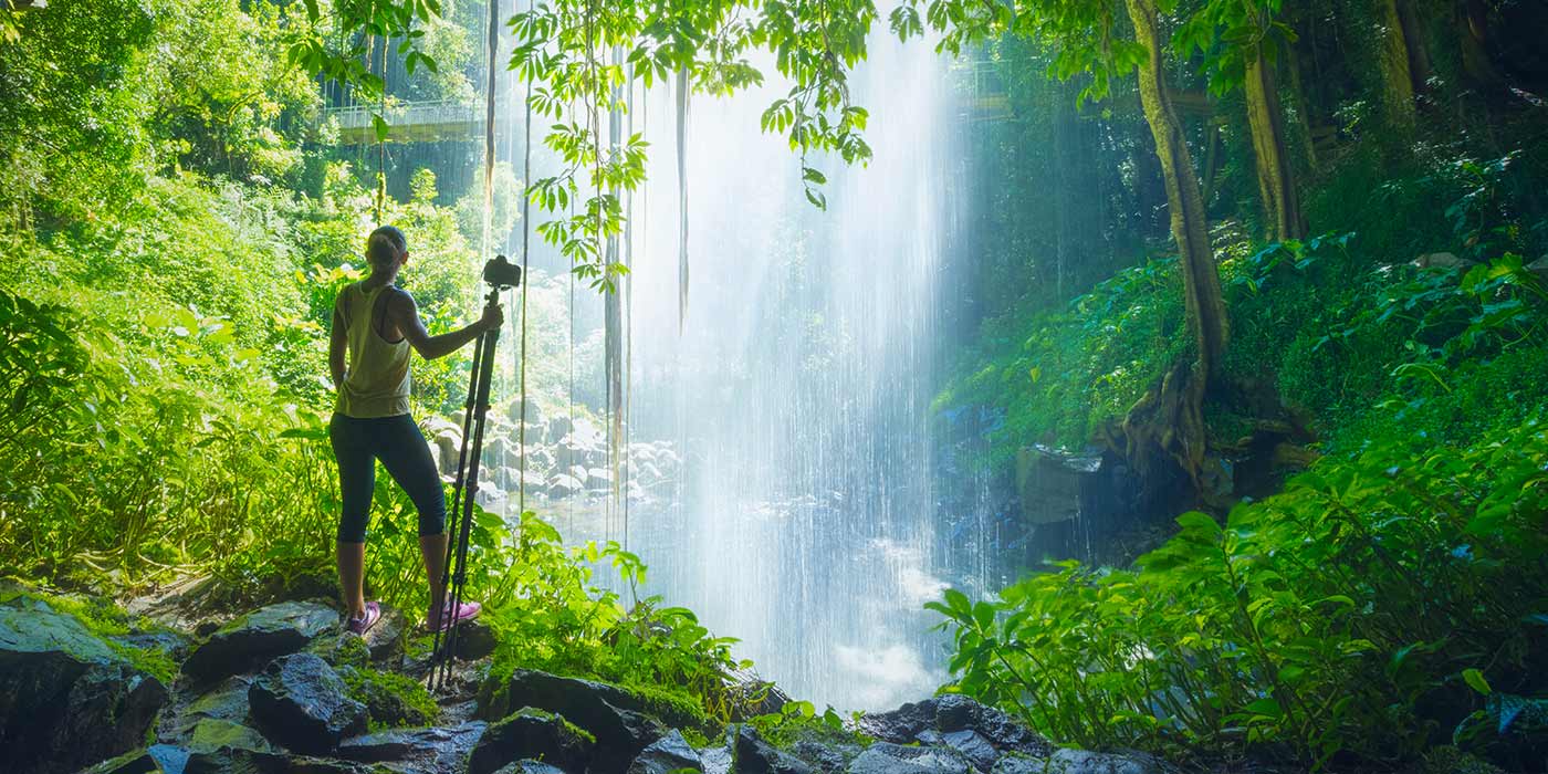 Hiking woman on an adventure holiday in Australia, standing in from of a waterfall in a rainforest.