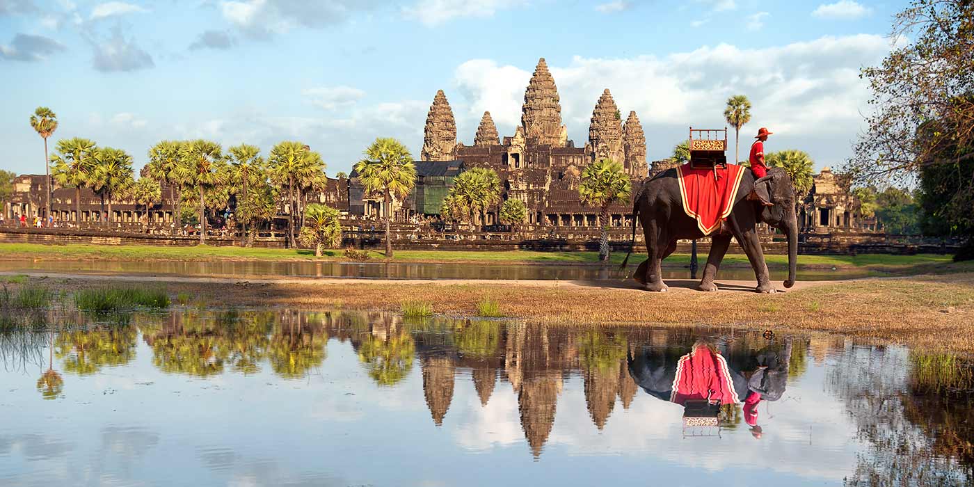 A tour of Siam Reap on tailor made holidays, with an elephant with a red blanket walking in front of the temple.