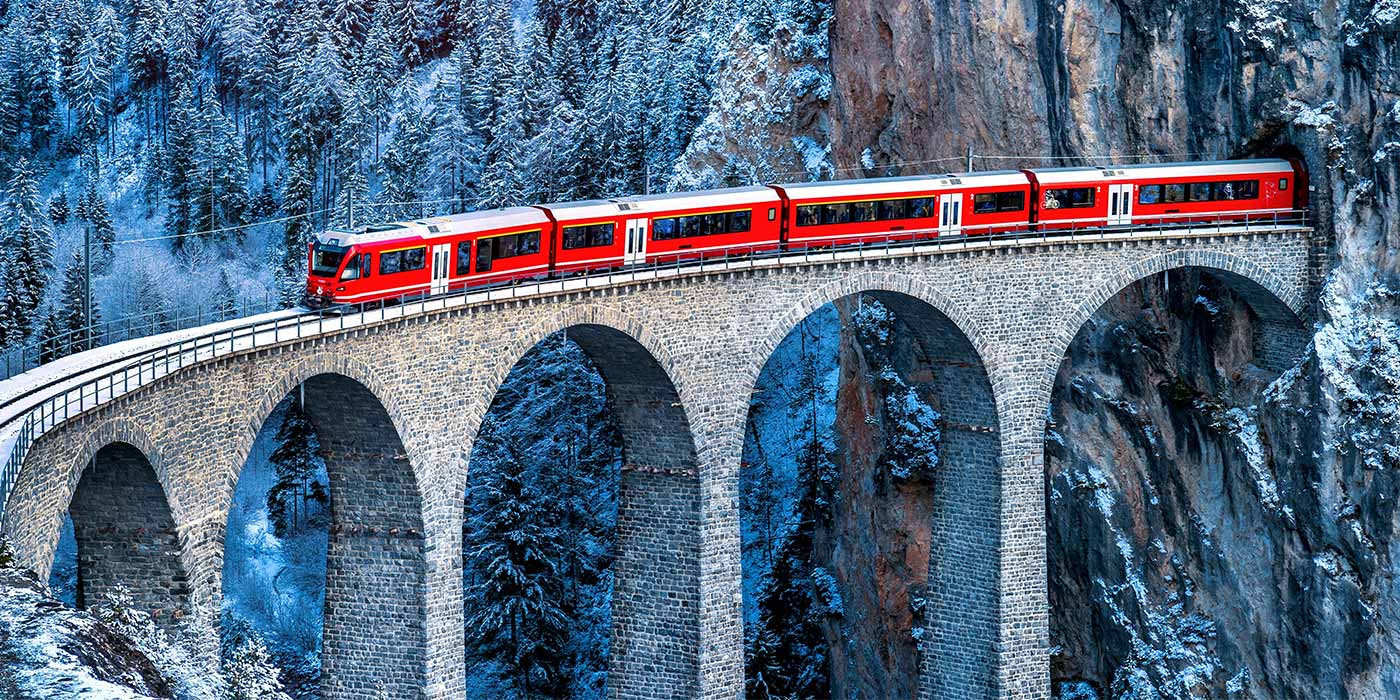 A train holidays europe tour passing through a mountain in snowy Switzerland.