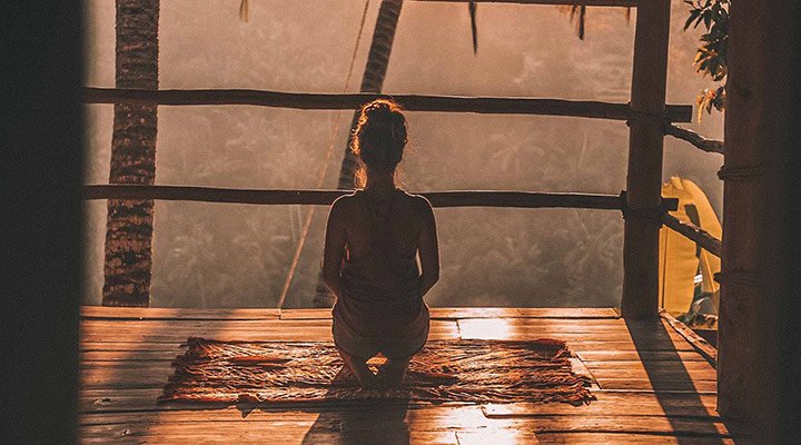 A woman sitting peacfully on the wooden deck of her villa in Bali on a wellness holiday.