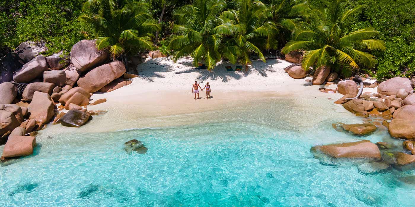 A couple on a luxury holiday standing on a tropical beach in the Seychelles.