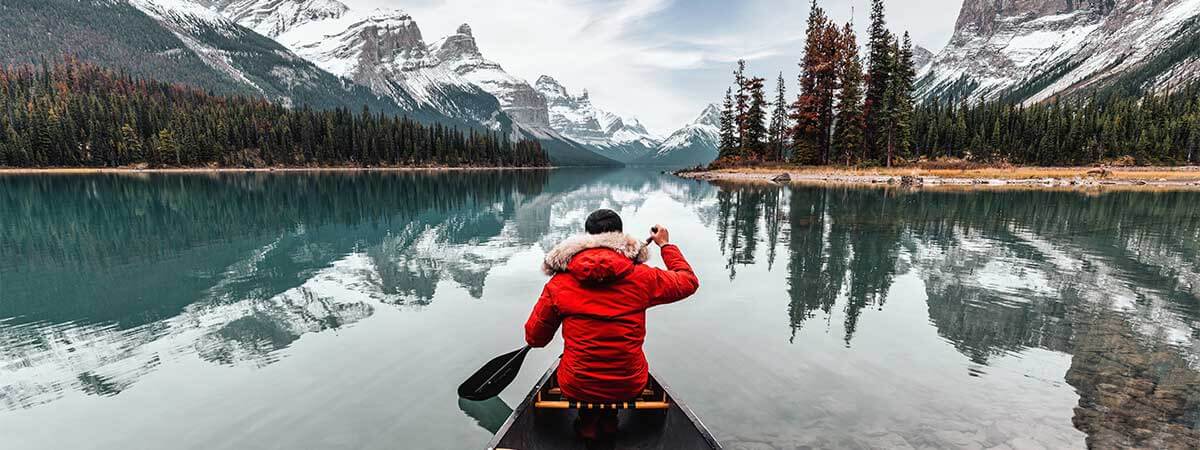 Kayaking through the great lakes on holiday in Canada, surrounded by snow-capped mountains.