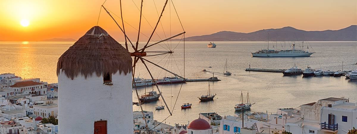 The sun setting over the ocean and behind a traditional windmill on holiday in Mykonos.