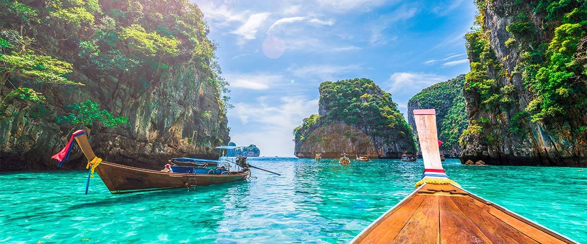 Thailand long boats in a turquoise sea, surrounded by mountains.