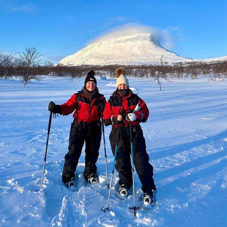 Holidaymakers in Lapland wearing ski suits and standing in front of a snow-capped mountain.