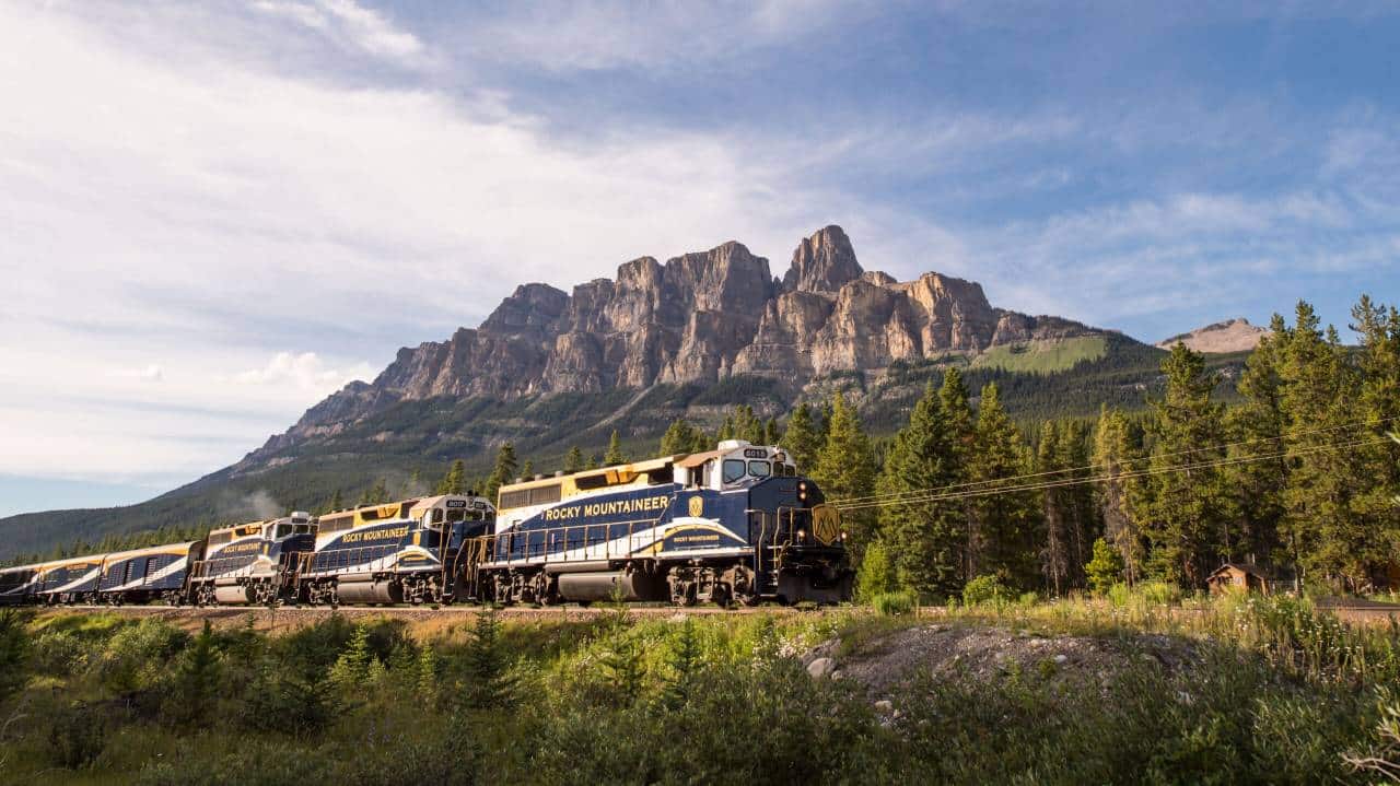 Rocky Mountaineer train passing through a picturesque mountain landscape with dramatic peaks in the background