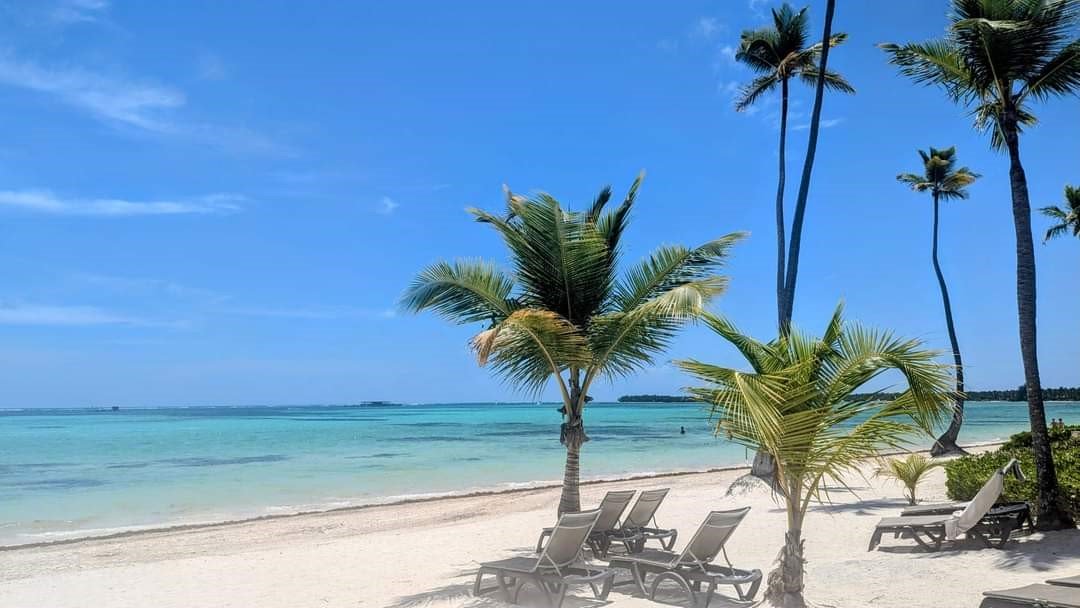 Pristine white sand beach with turquoise water, palm trees, and beach loungers under a clear blue sky