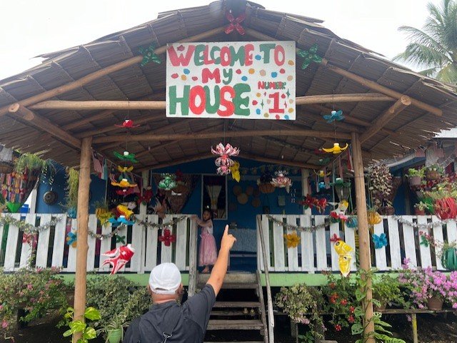 Colourful local home entrance with handmade 'Welcome to My House' sign, decorated with festive ornaments and white picket fence