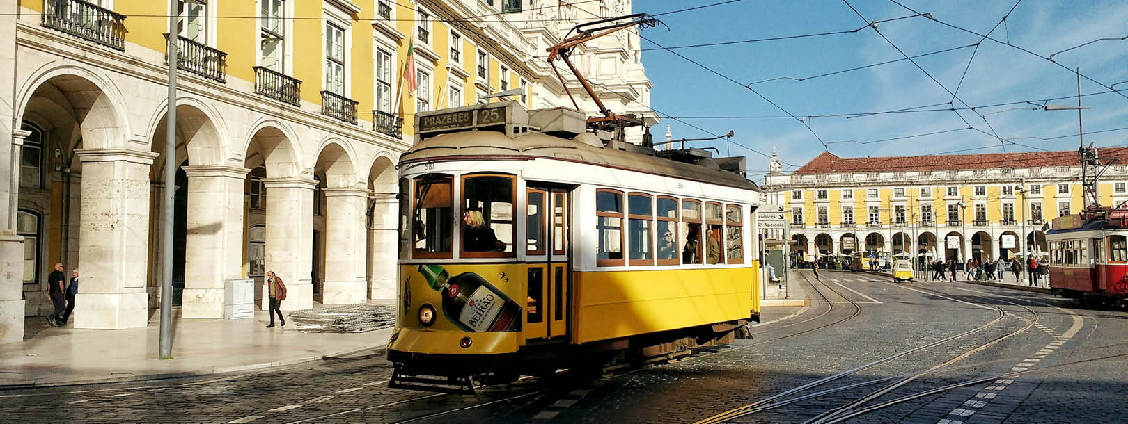 Traditional yellow tram passing through Praca do Comercio with classical Portuguese architecture featuring white stone arches and yellow buildings