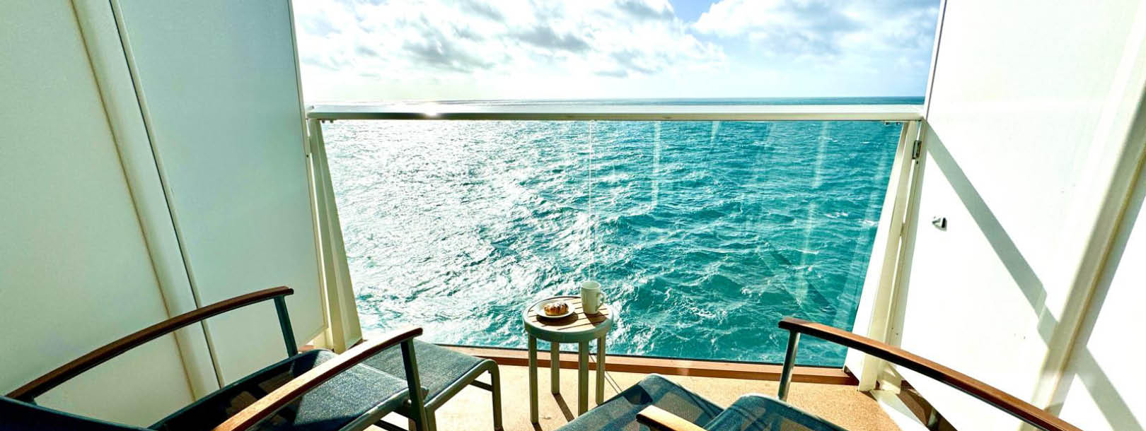 Private cruise ship balcony with two loungers overlooking turquoise ocean waters under bright sky