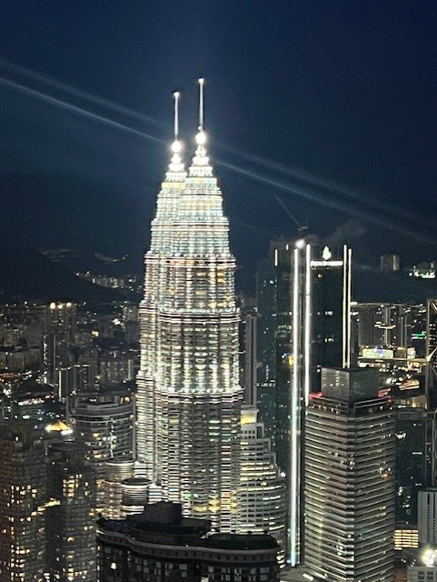 Petronas Twin Towers illuminated at night in Kuala Lumpur, glowing silver against dark sky with surrounding skyscrapers