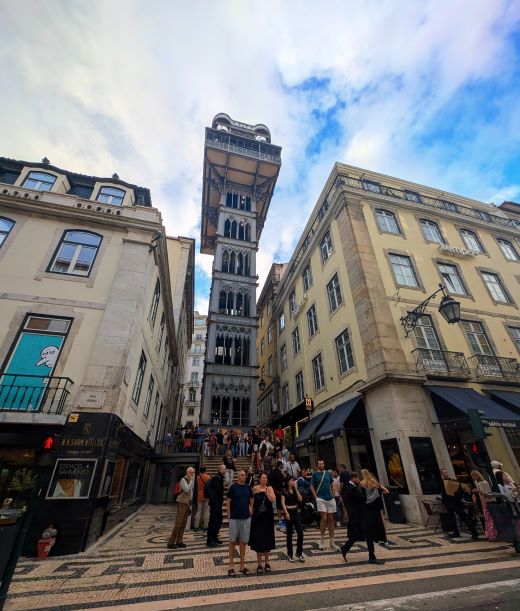 Historic Santa Justa Elevator towering between buildings in downtown Lisbon with tourists gathering at its base on decorative mosaic pavement