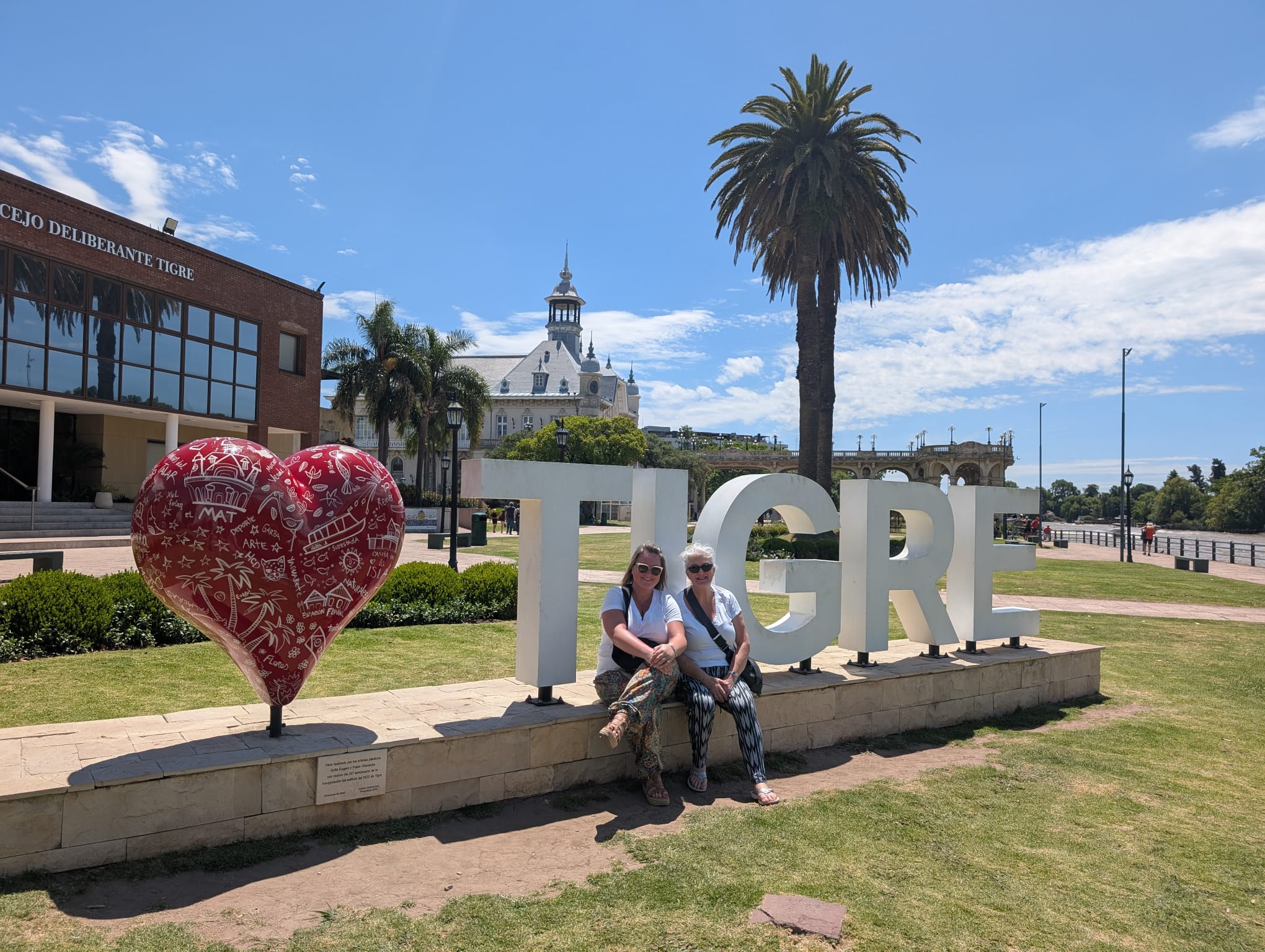Mother and daughter sitting on Tigre sign in Buenos Aires with decorative red heart sculpture