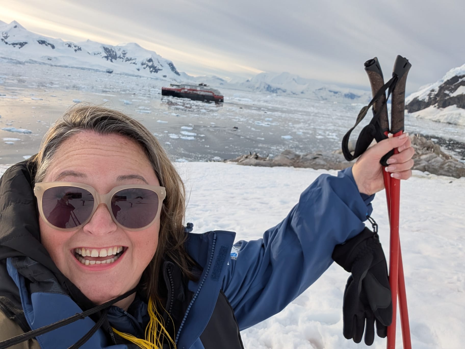 Woman smiling in Antarctica while snowshoeing, with expedition cruise ship visible in icy waters behind