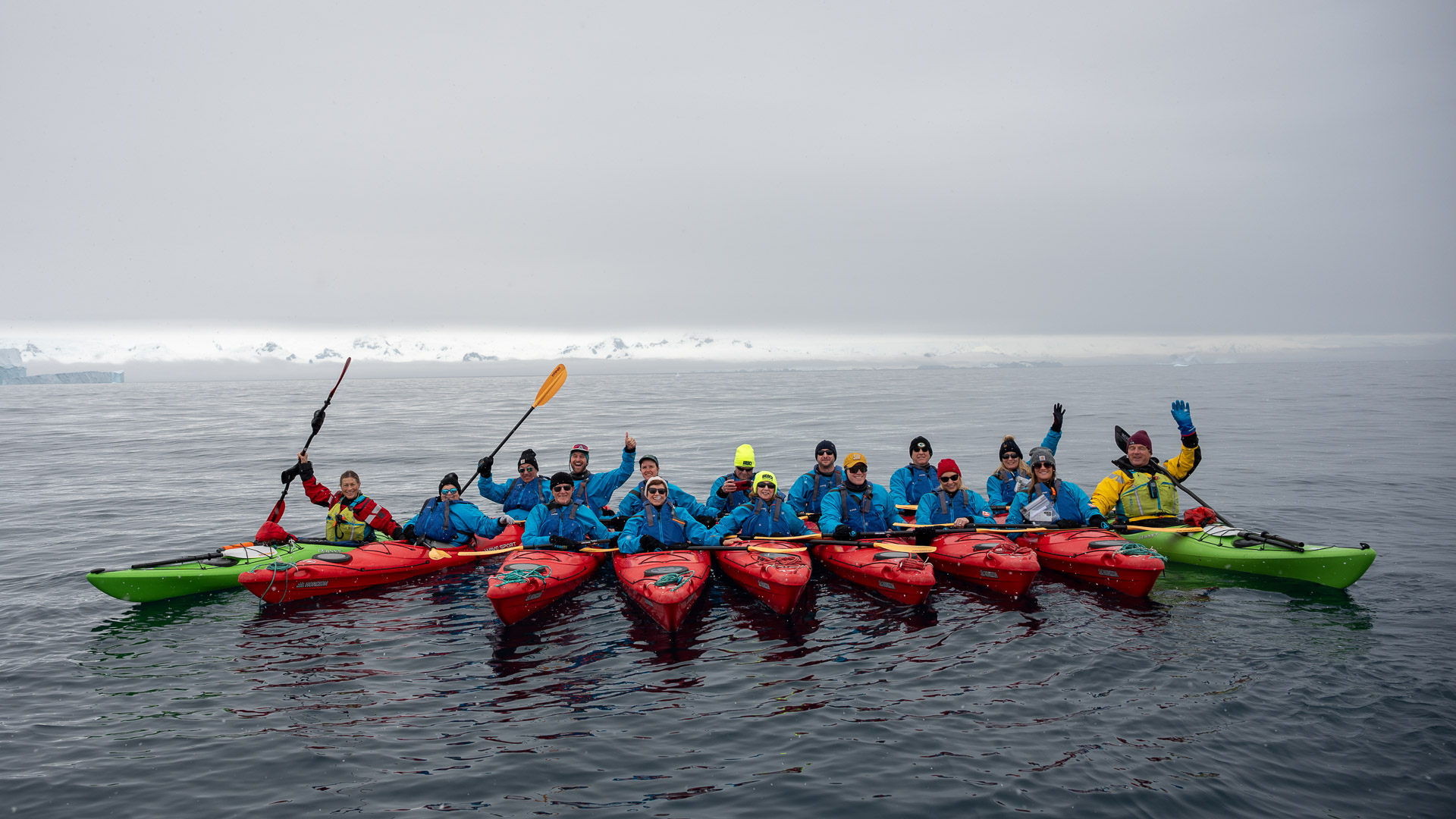 Group kayaking expedition in Antarctica with kayakers in red and green kayaks