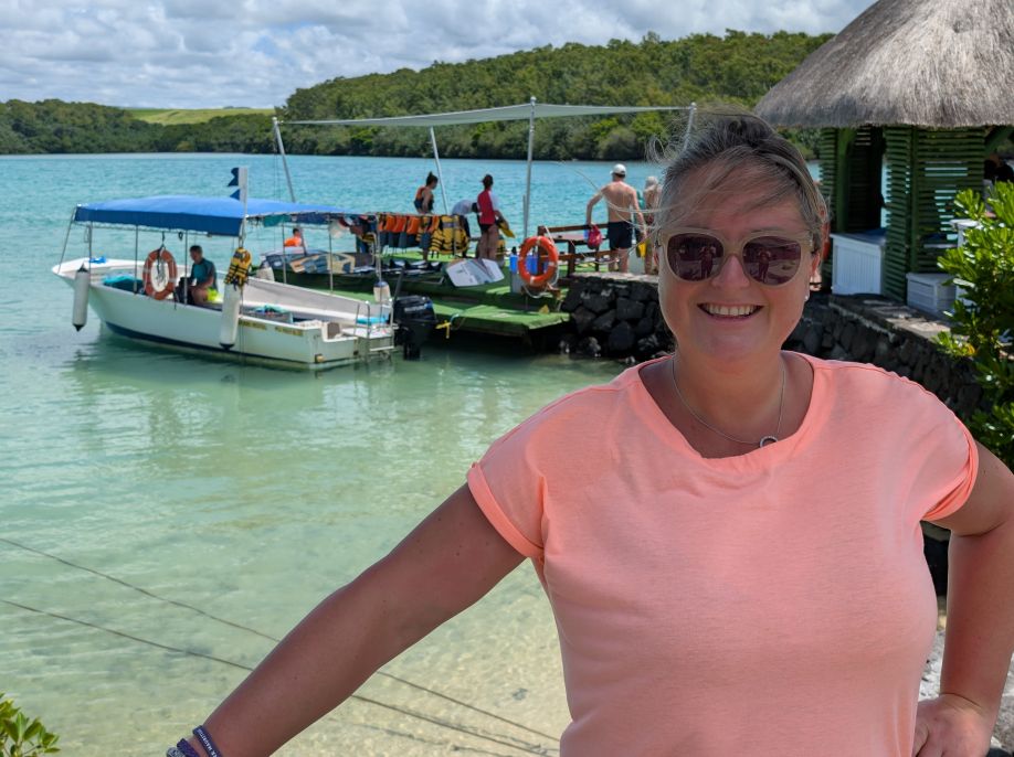 Smiling at a tropical island resort with turquoise waters and a boat dock in the background.
