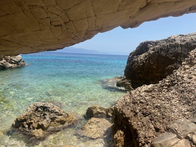 View from inside limestone cave overlooking crystal clear turquoise water and rocky Mediterranean coastline