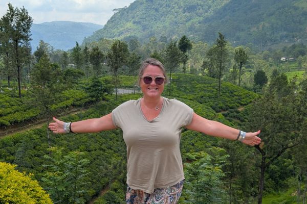 Woman with arms outstretched celebrating in Sri Lankan tea plantation with green hills and mountains