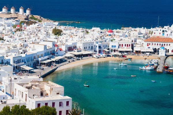 Greek island harbor with white Cycladic buildings, traditional windmills, and turquoise water with fishing boats