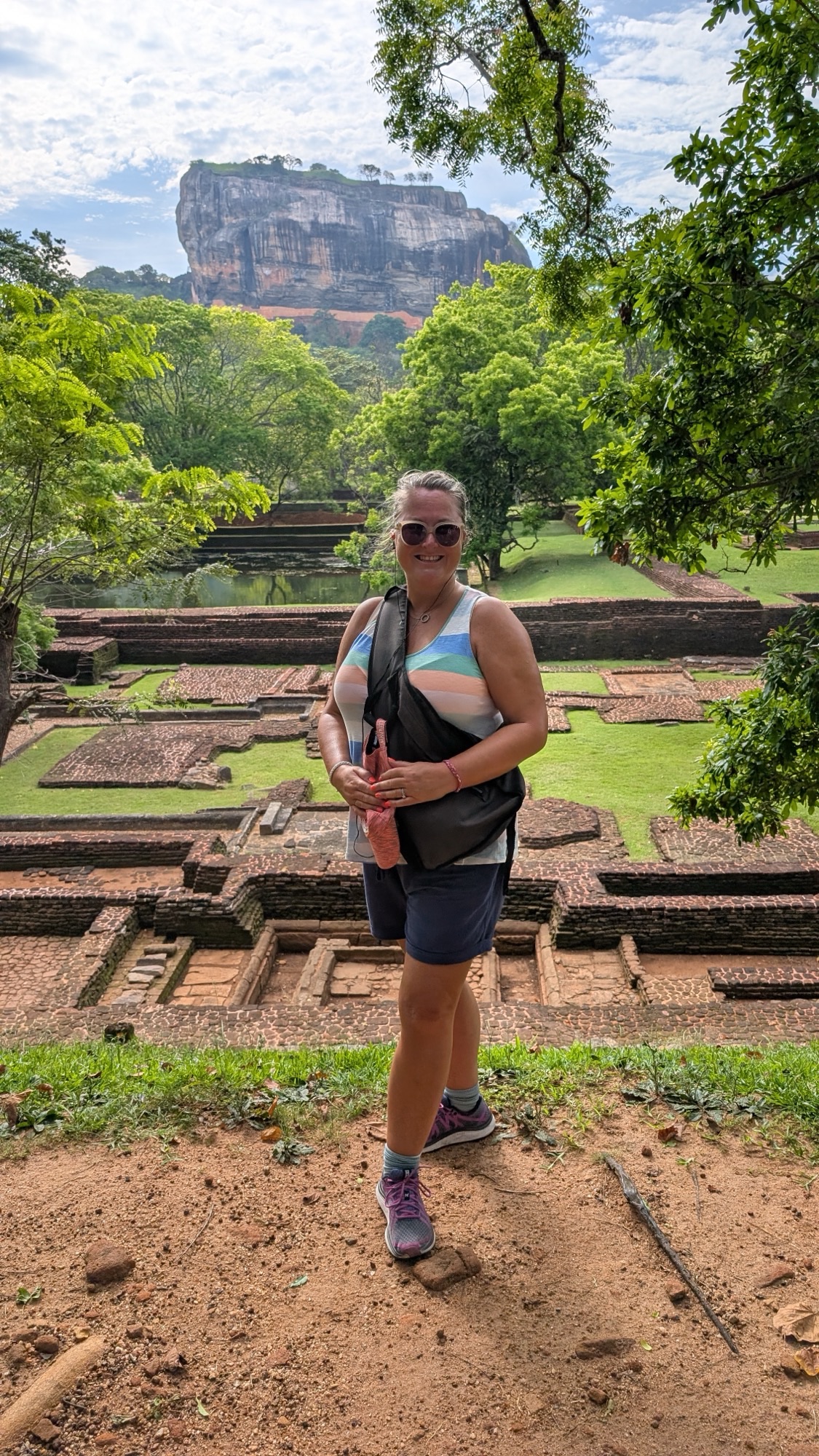 Woman standing among ancient ruins at Sigiriya archaeological site with Lion Rock fortress in background