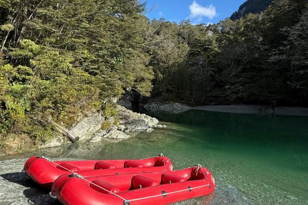 Red inflatable rafts on emerald green river surrounded by dense forest and rocky cliffs