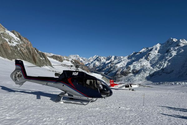 Black helicopter landed on snow-covered glacier surrounded by dramatic snow-capped mountain peaks